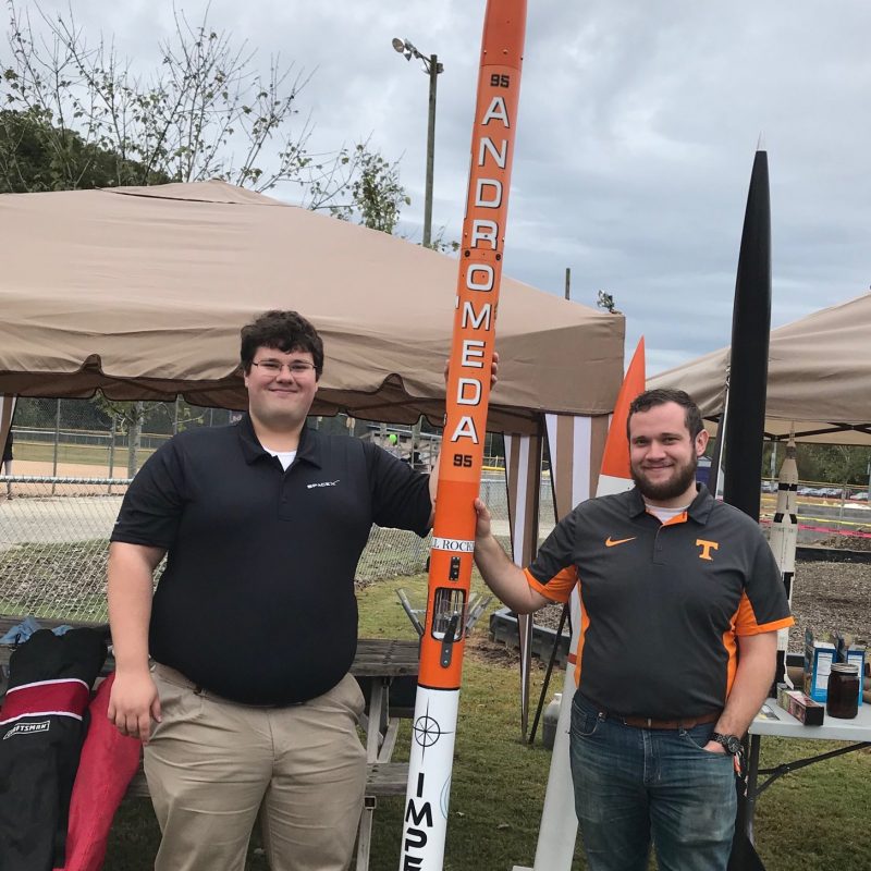 Two students stand next to amateur rocket