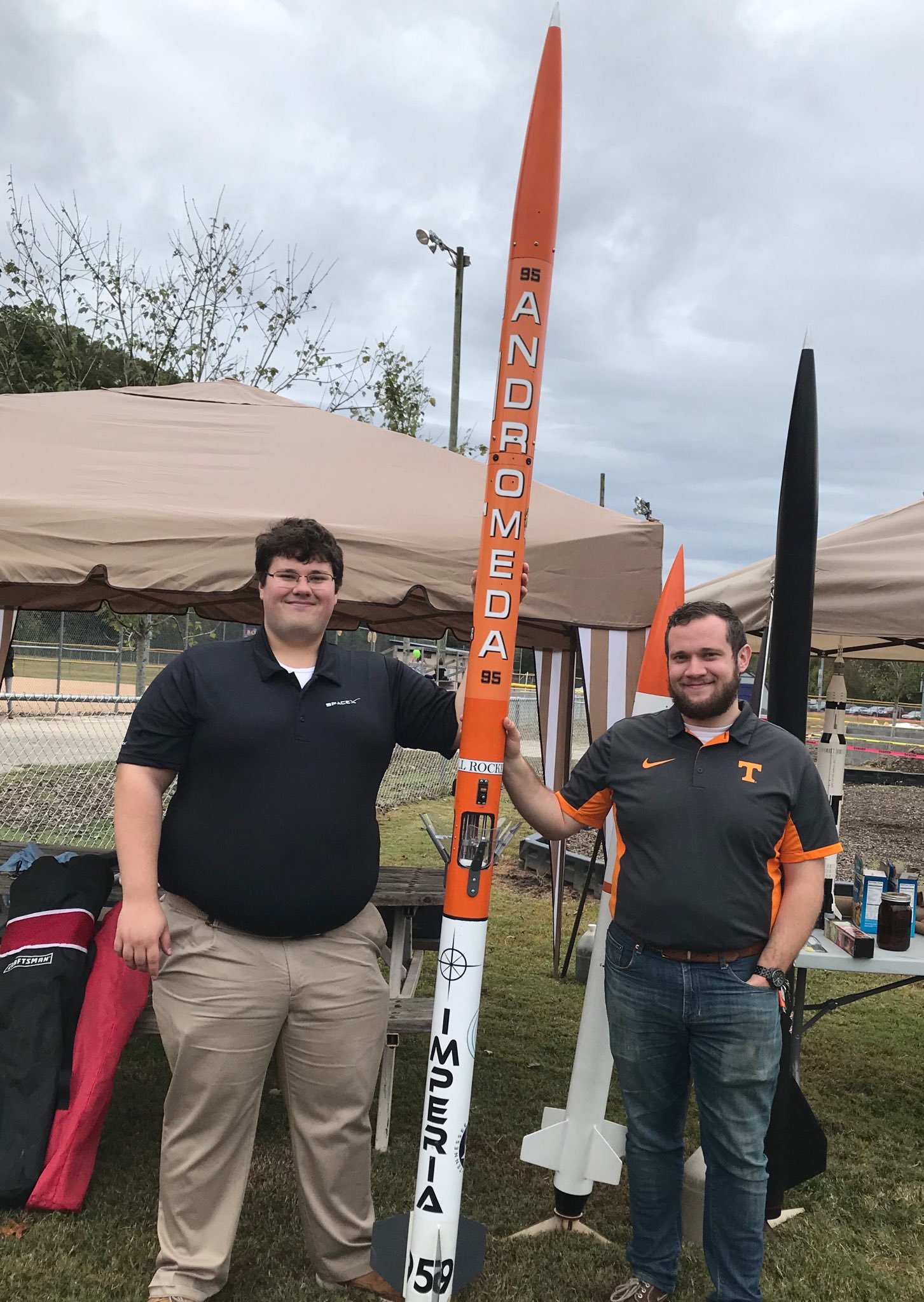Two students stand next to amateur rocket